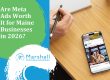 Are Meta Ads Worth It for Maine Businesses in 2026? - Person holding a pencil over a pad of paper in the top left corner and a phone with a Facebook ad in the bottom right corner